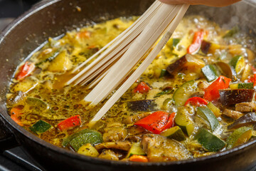 Frying pan with stewed vegetables in sauce and spices female hand puts udon.