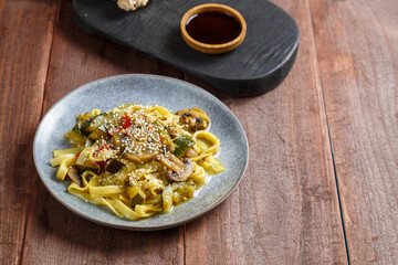 plate with udon vegetables mushrooms and sesame seeds on a wooden table.