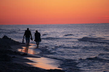 Para seniorów spacerująca brzegiem plaży o zachodzie słońca - obrazy, fototapety, plakaty