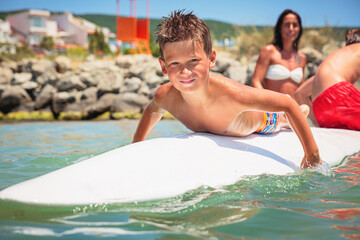 Cheerful teenage boy lying on a swimming board. Happy european family having fun floating on a swim board in the sea on a hot summer day