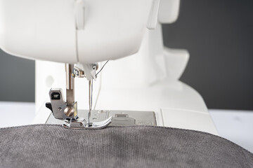 Modern sewing machine presser foot with gray fabric and thread, closeup. Sewing process clothes,...