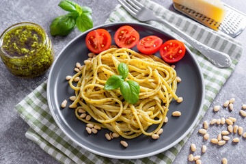 Pasta spaghetti with pesto sauce and fresh basil leaves in black bowl on gray concrete background served with food ingredients. Traditional italian cuisine.