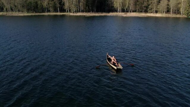 A lonely man oaring the boat at middle of lake.