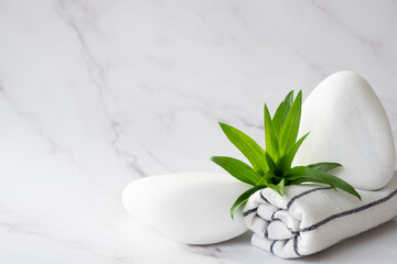 Obraz na płótnie Canvas SPA background concept. White stones, towel, and leaves of green plant on marble background with copy space. Body care and beauty treatment. Spa and wellness or beauty salon concept. Copy space.
