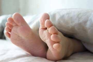 Feet under a light blanket on the bed. Concept of sleeping or waking in the morning