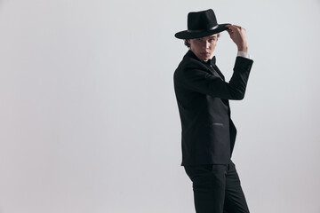 side view of sexy groom in black tuxedo fixing and adjusting hat