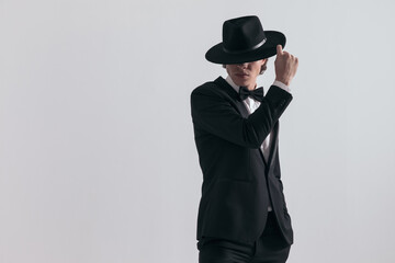 sexy fashion guy in black tuxedo covering forehead and eyes with hat