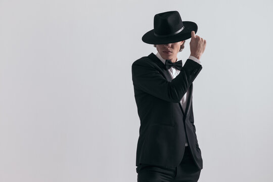 sexy fashion guy in black tuxedo covering forehead and eyes with hat