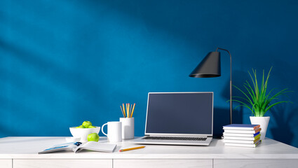 Interior of a modern home office with laptop against a blue wall with copy space