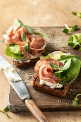 Bruschetta with ham or prosciutto, cream cheese, cucumber, spinach and microgreens. Tasty sandwich or toasted bread on wooden rustic board. Appetizer or breakfast