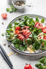 Green salad with ham or prosciutto, corn salad leaves, tomatoes and cheese close up. Healthy diet lunch on white marble background