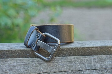 one men's fashionable durable leather belt with iron buckle lies on a wooden surface during the day outdoors in summer