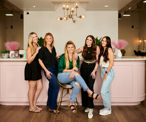 Fototapeta premium CONROE, TEXAS, USA - APRIL 14th 2023: 5 female managers of a beauty salon are posing for a business portrait in the salon against their company logo. Thel have professional makeup and hair extensions