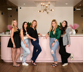 CONROE, TEXAS, USA - APRIL 15th 2023: 5 female managers of a beauty salon are posing for a business portrait in the salon against their company logo. Thel have professional makeup and hair extensions