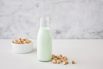 Pistachio milk in a bottle on a gray table next to pistachios. Plant milk
