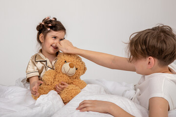 Funny children sister and brother playing on bed, happy cute little child girl and her brother having fun in bedroom enjoying family leisure morning lifestyle activity together at home