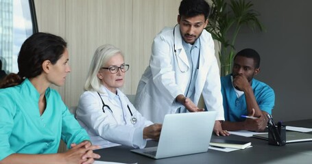 Multiracial team of medical employees, mature and young professional working together in conference room use laptop, discuss diagnose, reviewing checkup results. Concilium event of diverse therapists
