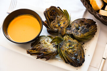 Delicious grilled artichoke halves served with romesco sauce on plate