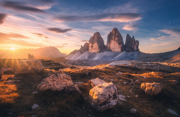 Rocks and stones at sunset in autumn in Tre Cime, Dolomites, Italy. Colorful landscape with mountains, trail, orange grass, blue sky with clouds, golden sunlight in fall. Hiking in mountains. Nature