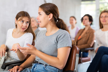 Young girls are sitting in lecture hall and enthusiastically whispering about latest news of university. malicious talk , conversation, communication , trust, happiness, gossip