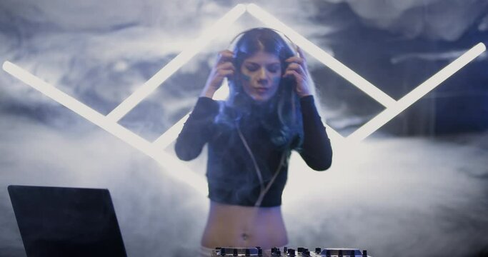 Female DJ playing on a mixer. Girl mixing trance music. Futuristic shape of LED tubes and smoke in the background.