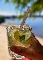 popular mojito green rum cocktail in hand with ocean in background