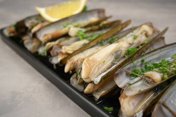 dish of razor clam grilled with garlic, parsley, olive oil and lemon slice on wood table