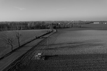 farmer driving a crawler tractor drags a cloud of dust behind, ploughing, power harrowing surface...