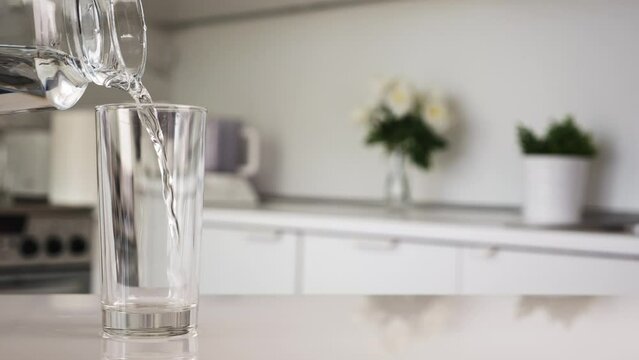 Pouring clean water from jug in glass at the kitchen, closeup
