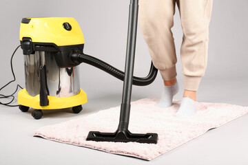 Woman hoovering carpet on grey background, closeup