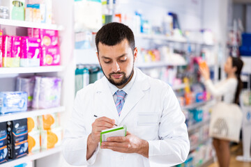 Young adult man pharmacist holding notepad and pen working at pharmacy