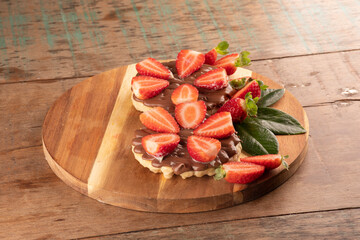 dessert of two waffles with chocolate and hazelnut cream on round wooden board on wooden table.in...