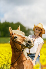 Portrait of a young equestrian woman riding her haflinger horse through a field of canola flowers...