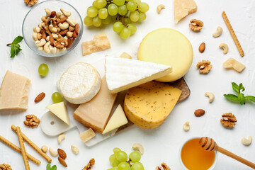 Board with different types of tasty cheese, grapes, nuts and honey on light background