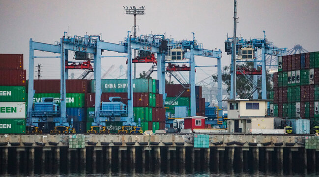 San Pedro, California USA - November 7, 2021: On a foggy evening, large mobile cranes position shipping containers along a pier in the Port of Los Angeles.