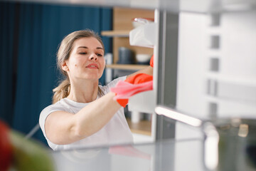 Woman in red gloves is doing cleaning and wash a refrigerator inside