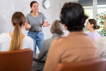 Fototapeta premium Positive friendly young girl giving lecture to group of women of different ages during educational class..