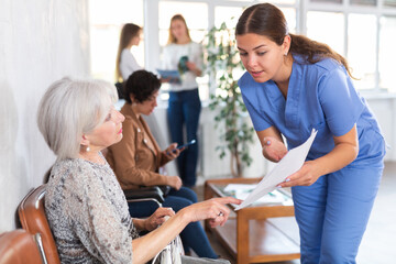 Polite young woman in blue uniform, professional medical worker, showing documents and explaining...