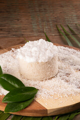 coconut cake with icing and shredded coconut on wooden board on tropical rustic table close-up