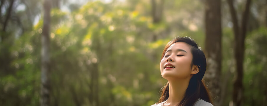 A Oriental woman standing in a forest with her eyes closed