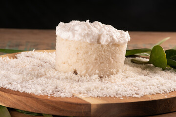 coconut cake with icing and grated coconut on wooden board on rustic table in front close-up