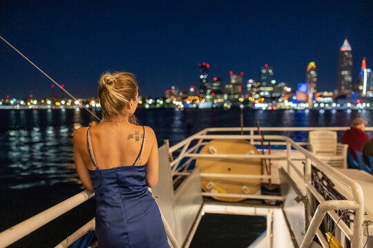 Young woman on a boat viewing the illuminated Cleveland skyline in the background. 