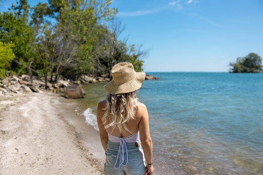 Young woman with tropical hat on the beach looking into the ocean 