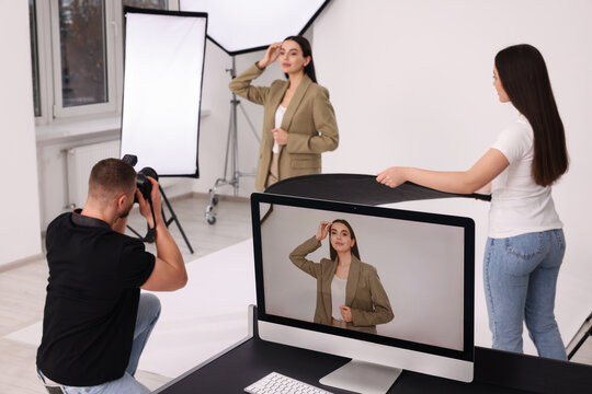 Professional photographer and assistant working with beautiful model in modern photo studio, selective focus