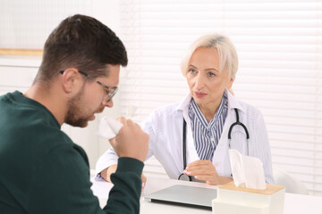 Sick patient with napkin and doctor at table in clinic