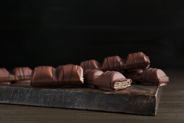 Tasty chocolate bars on wooden table against black background