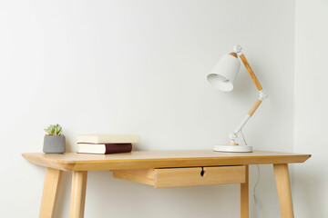 Stylish lamp, books and houseplant on wooden table near white wall. Interior design