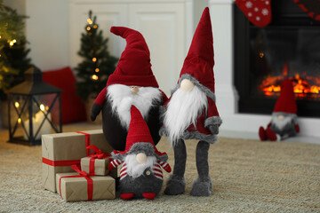 Obraz premium Funny Christmas gnomes with gift boxes on floor near fireplace indoors