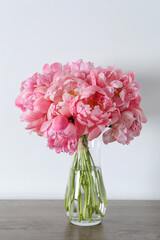 Beautiful bouquet of pink peonies in vase on wooden table against white background