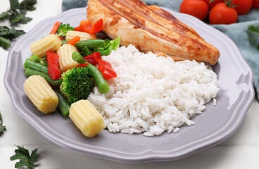 Grilled chicken breast and rice served with vegetables on white table, closeup